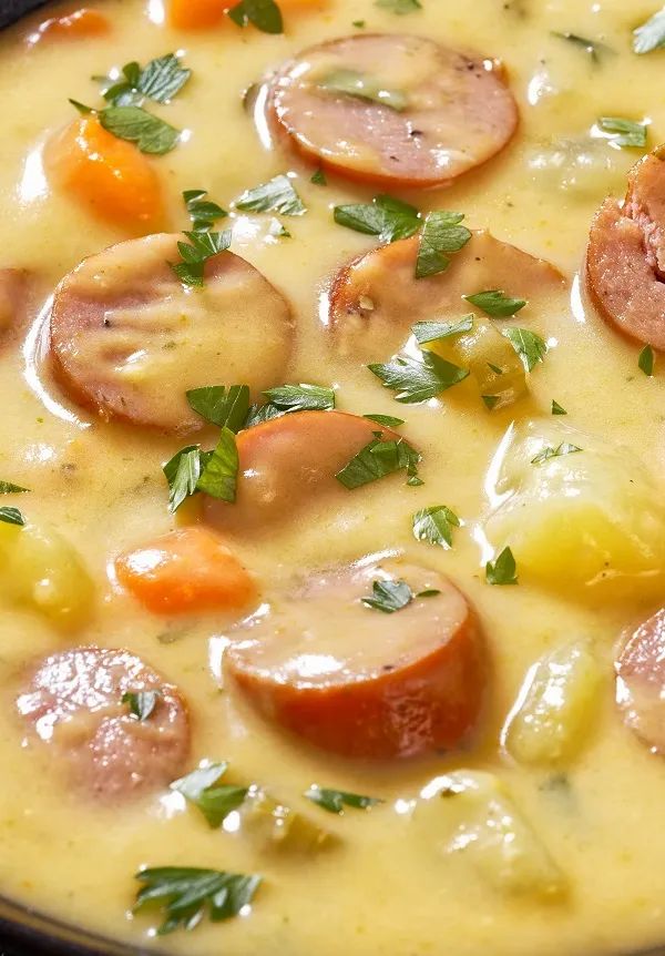 a close up of a bowl of soup with sausages and carrots in it