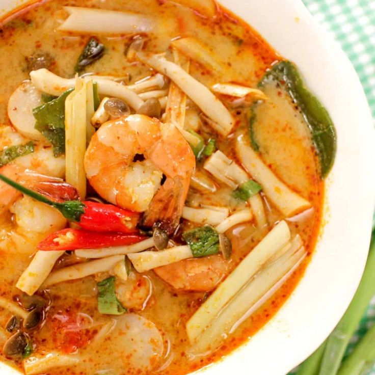 a white bowl filled with shrimp and vegetable soup on top of a green table cloth