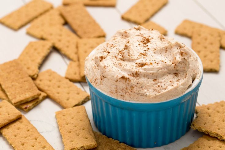 a blue cup filled with whipped cream surrounded by crackers on a white tablecloth