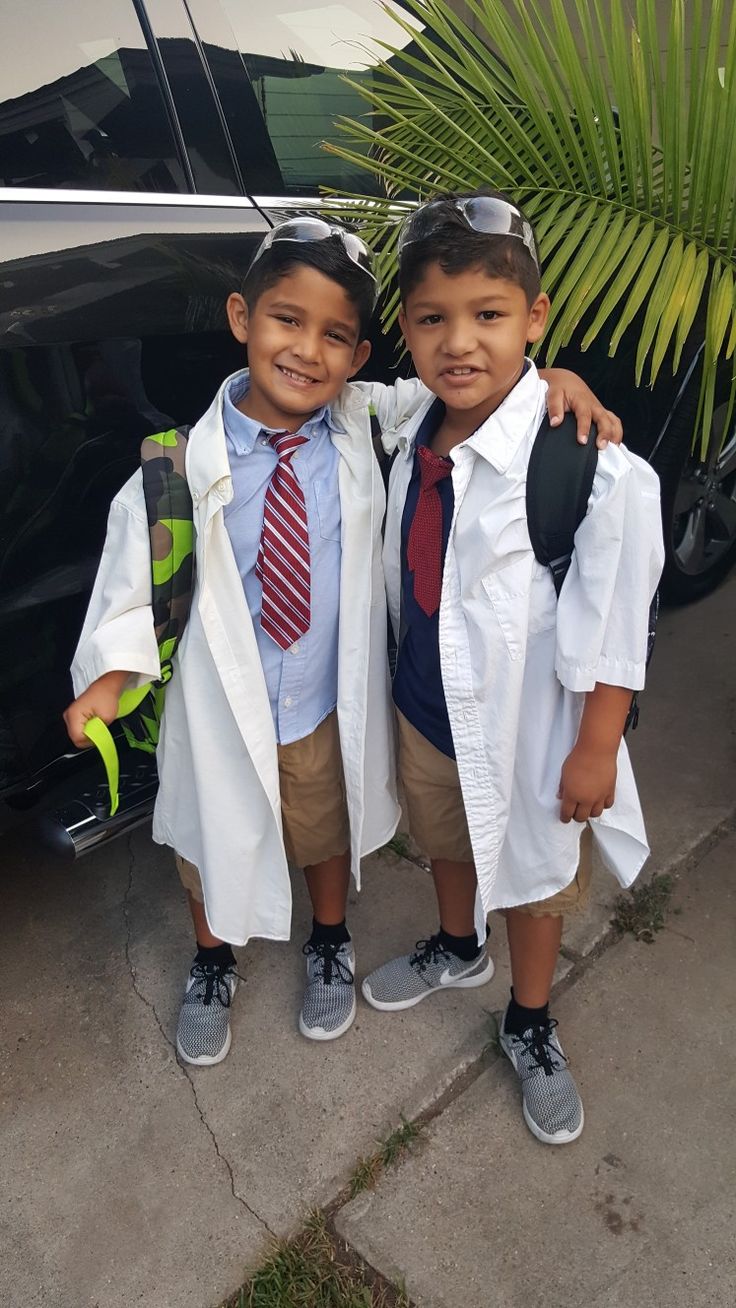 two young boys wearing lab coats and ties standing next to each other in front of a car