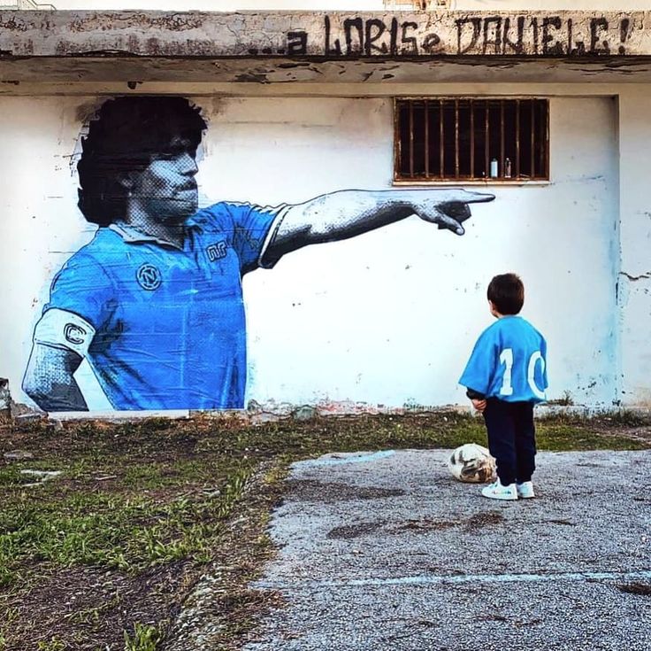 a young boy standing in front of a wall with a painting of a soccer player on it