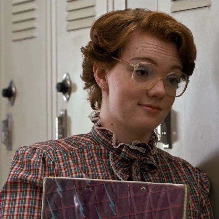 a woman with glasses holding a box in front of lockers