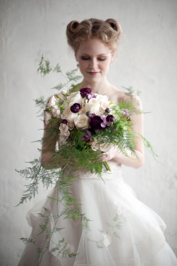 a woman in a white dress holding a bouquet of purple and white flowers on her wedding day