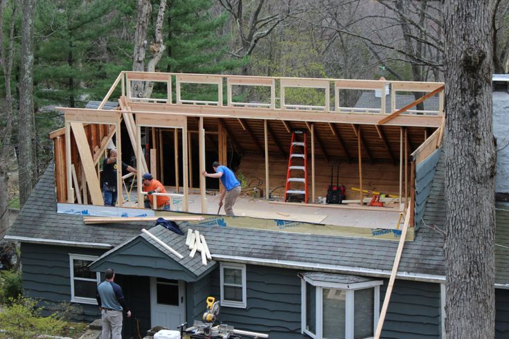 two men are working on the roof of a house that is being built in the woods