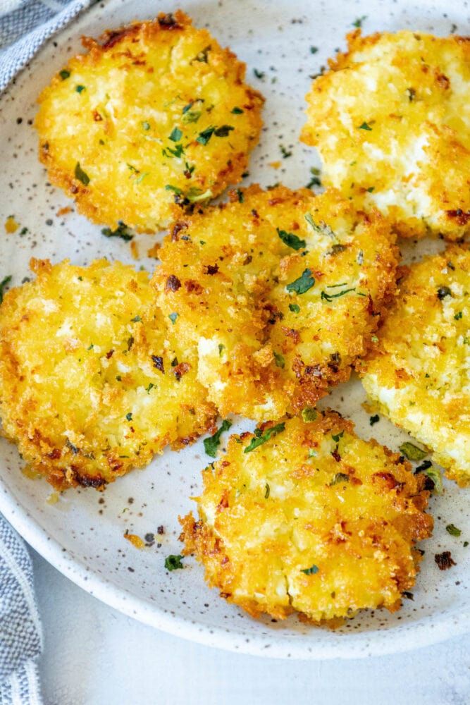 four crab cakes on a white plate with parsley sprinkled on top, ready to be eaten