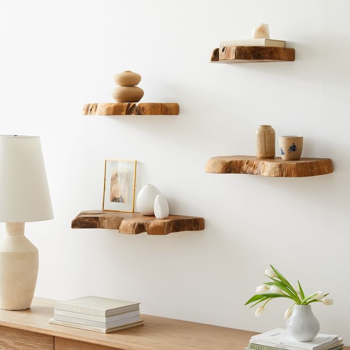 three wooden shelves on the wall above a table with a lamp, vase and other items