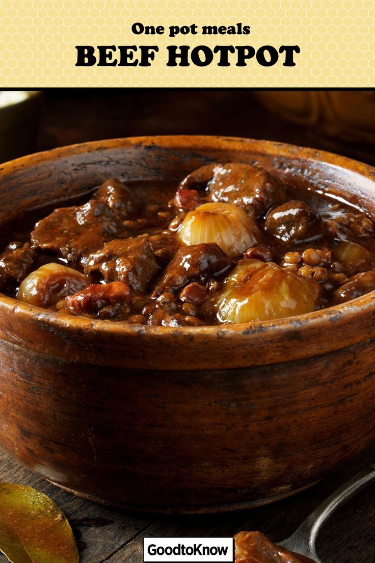 a wooden bowl filled with beef and potatoes on top of a table next to spoons