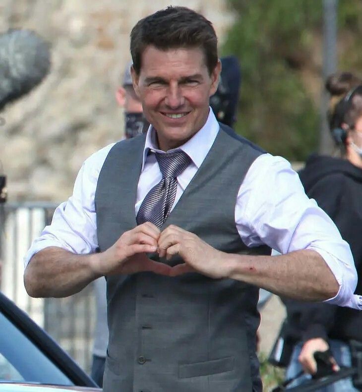 a man in a vest and tie standing next to a car