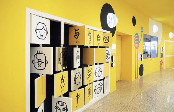 a hallway with yellow walls and black and white drawings on the wall, along with several lockers