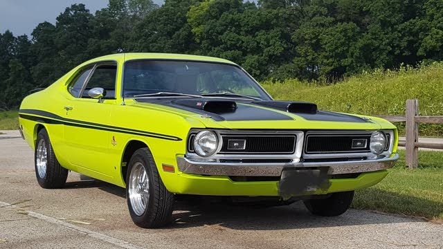 a bright yellow muscle car parked in a parking lot next to a wooden fence and trees