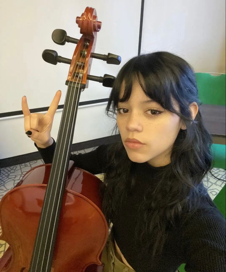 a woman sitting on the floor with a violin in front of her and pointing at the camera