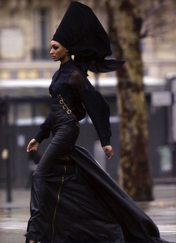 a woman is walking down the street in a black dress and head scarf, with an umbrella over her head