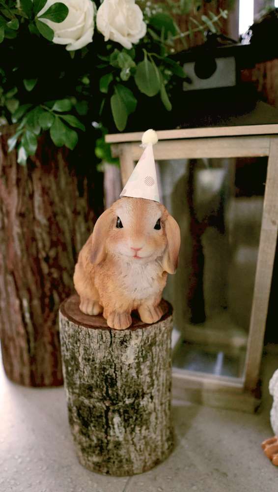 a small rabbit figurine sitting on top of a tree stump wearing a party hat