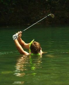 a woman is in the water holding onto a golf club and trying to hit it