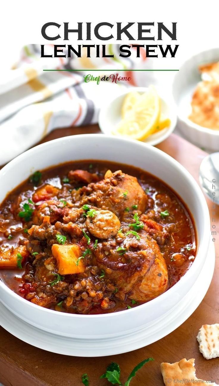 chicken lentil stew in a white bowl with crackers and lemon wedges on the side