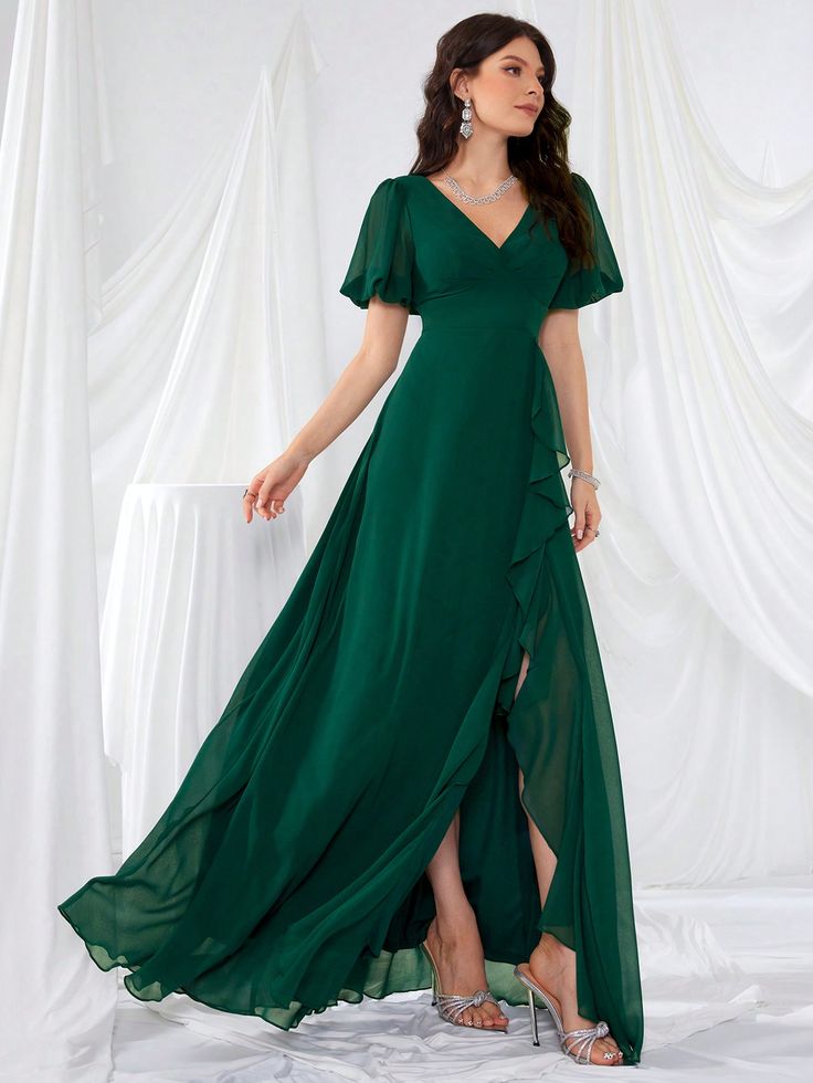 a woman in a long green dress standing on a white backdrop with her legs crossed