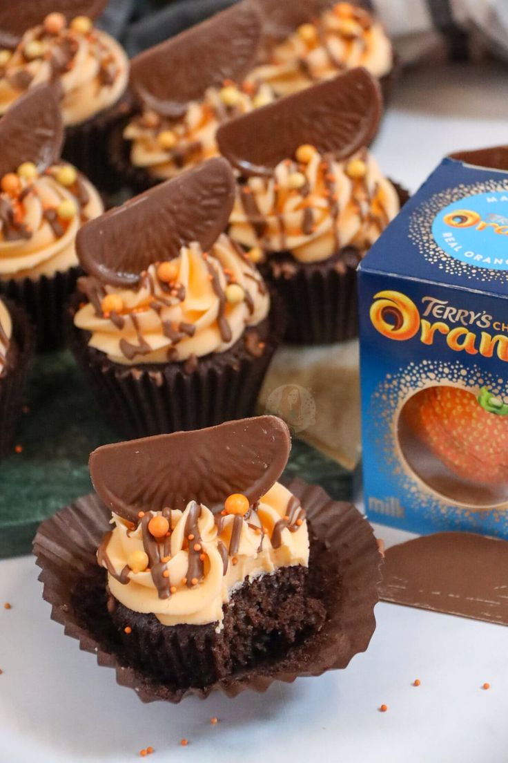 chocolate cupcakes with frosting and nuts on top next to a box of orange zest