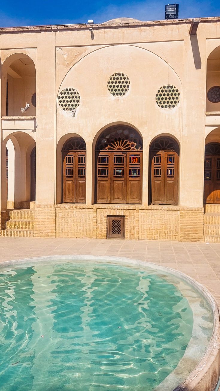 an outdoor swimming pool in front of a building with arched doorways and doors on each side