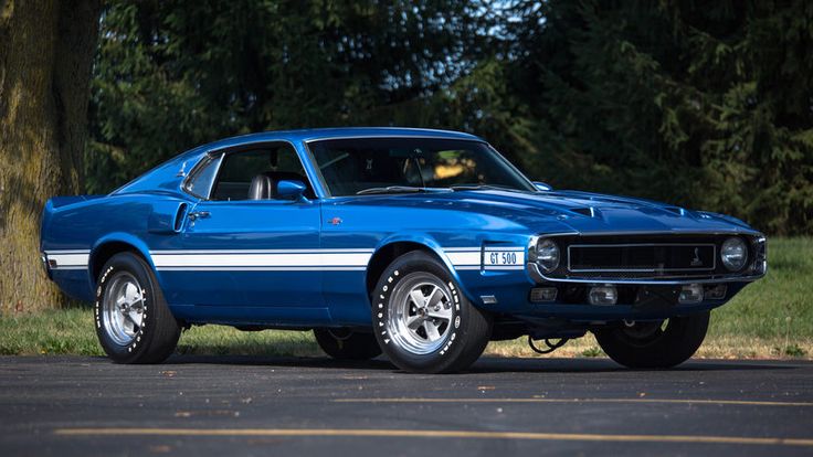 a blue muscle car parked on the side of the road in front of a tree