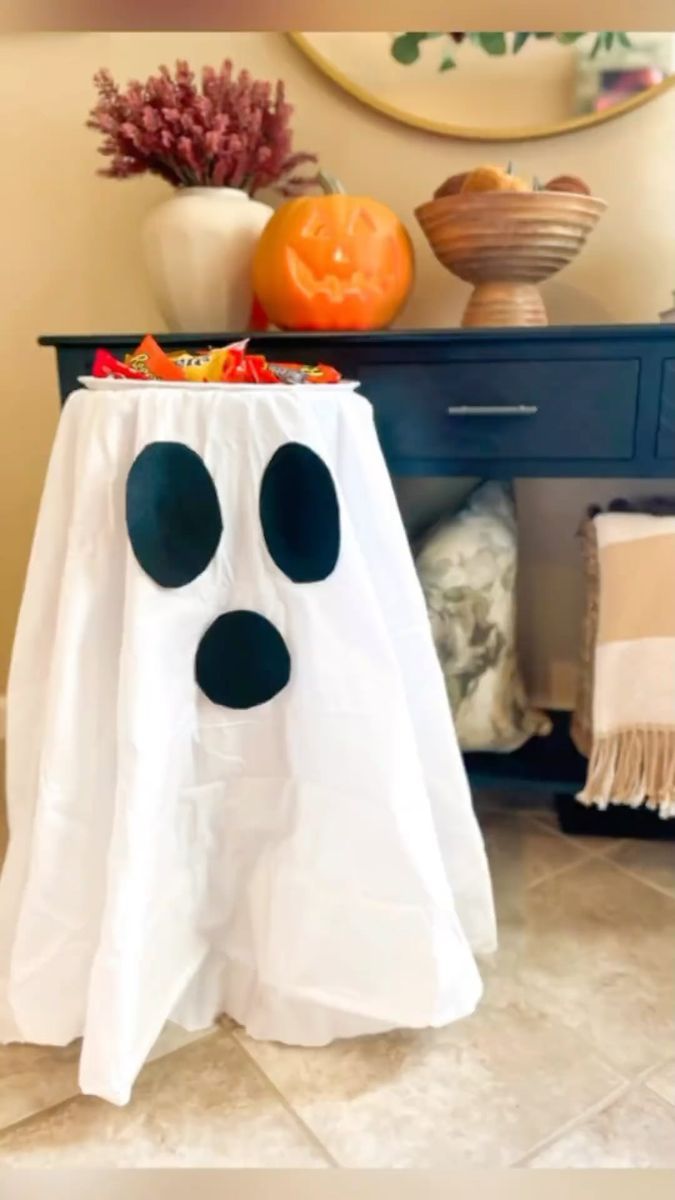 a white table topped with a black and white ghost cloth covered in fake pumpkins