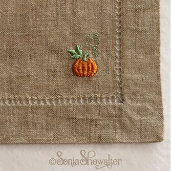 a small embroidered pumpkin sitting on top of a piece of cloth with stitching around it