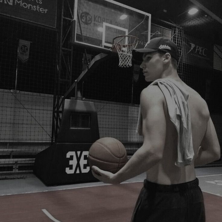 a young man holding a basketball on top of a basketball court in an indoor gym