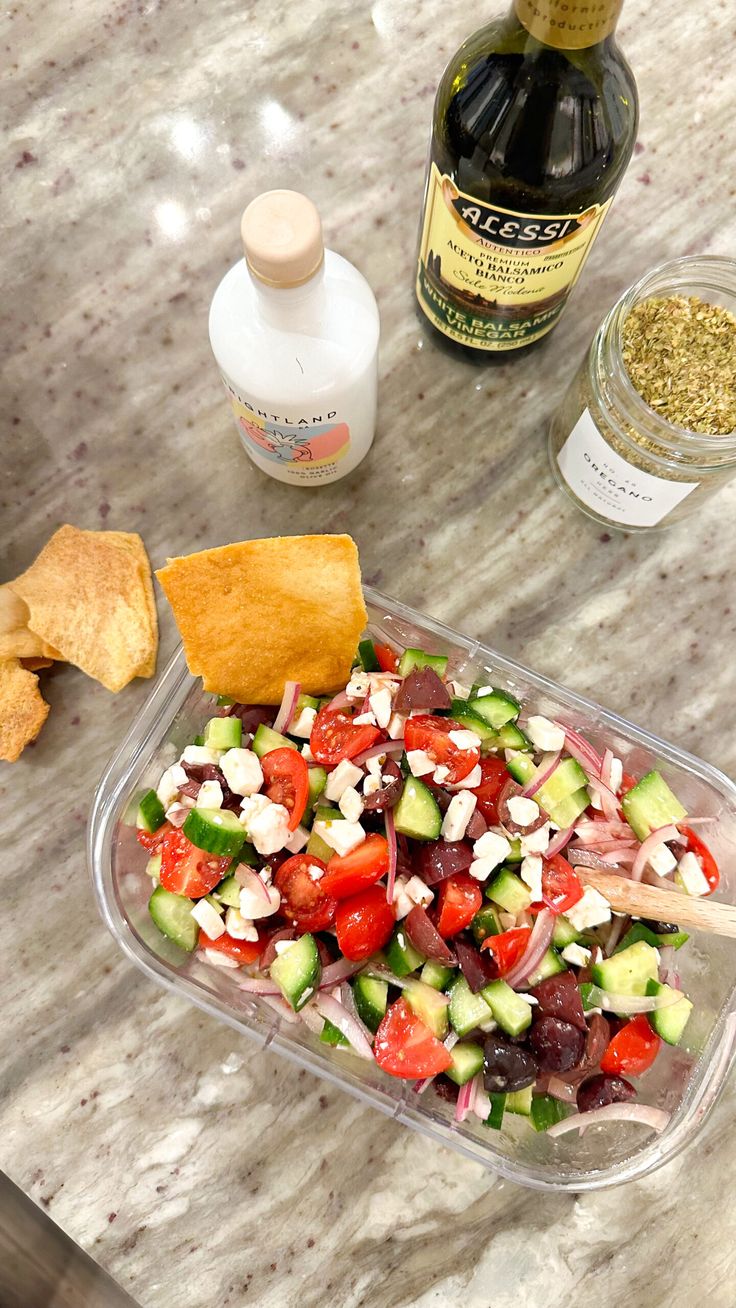 a salad with cucumbers, tomatoes and other vegetables in a plastic container on a marble counter top