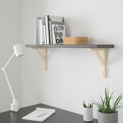 a desk with a lamp and some books on the shelf next to it is a potted plant