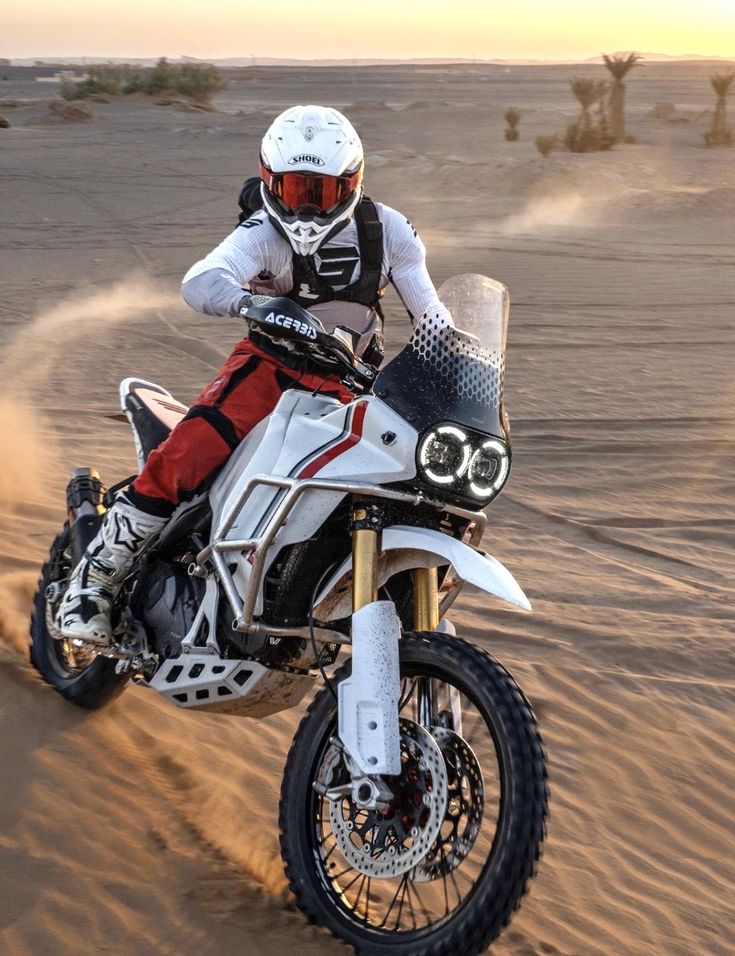 a man riding on the back of a white dirt bike in the middle of desert