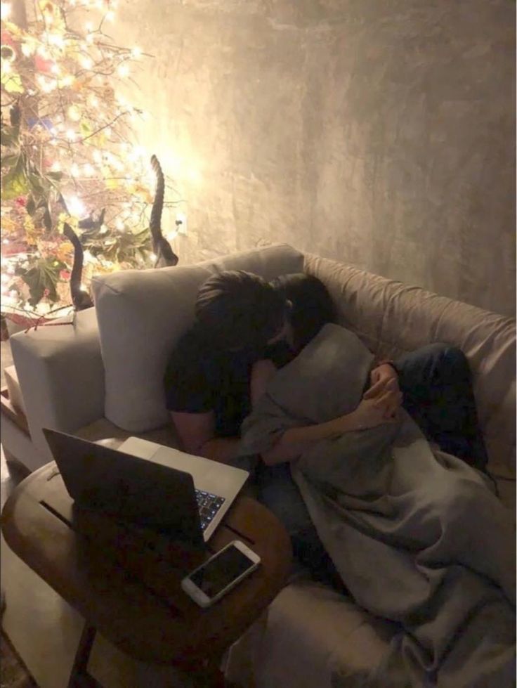 a person is sleeping on a couch with a laptop in front of a christmas tree