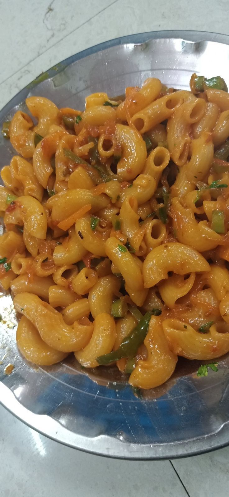 a silver plate filled with pasta and vegetables on top of a white marble countertop