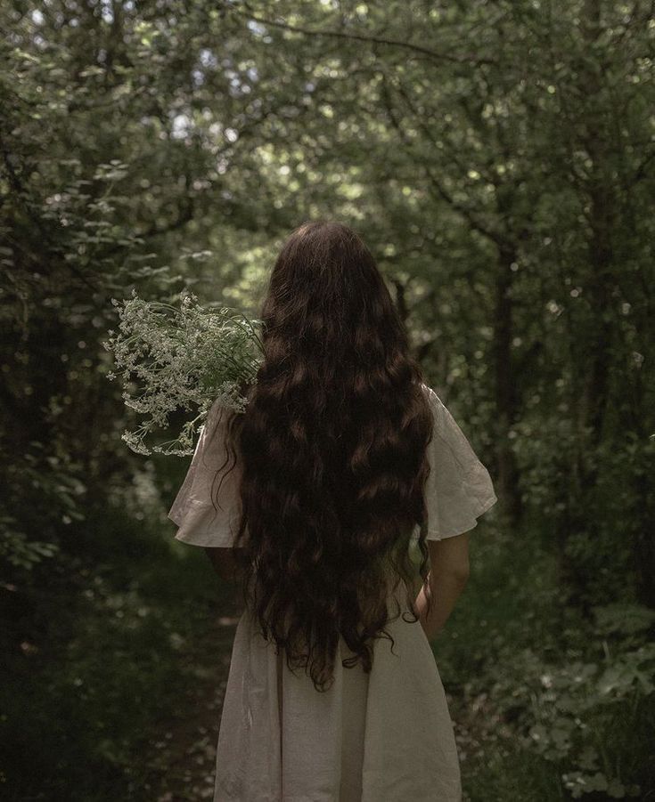 a woman with long hair standing in the middle of a forest looking back at something