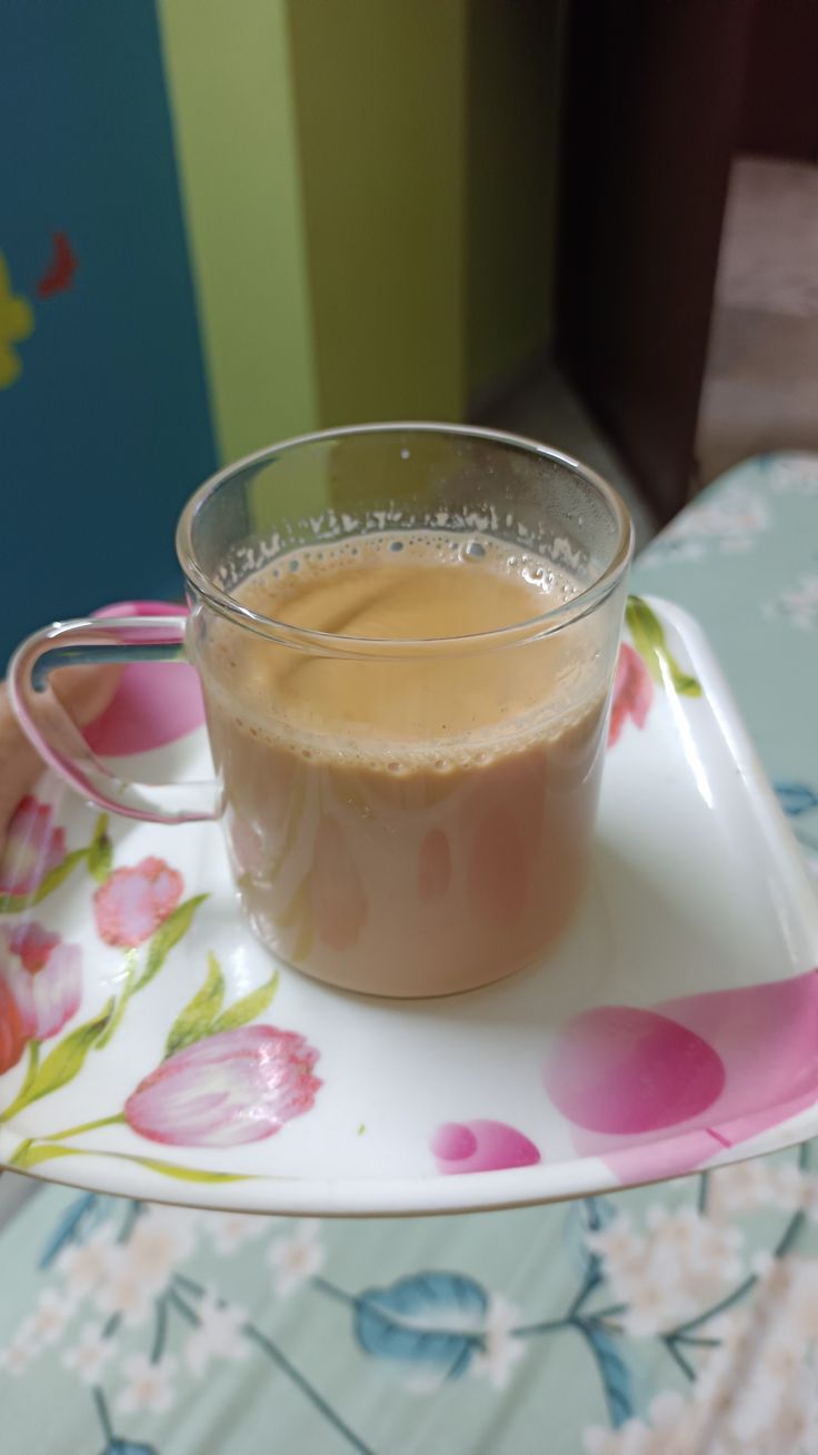 a cup of coffee sitting on top of a white plate next to a flowered table cloth