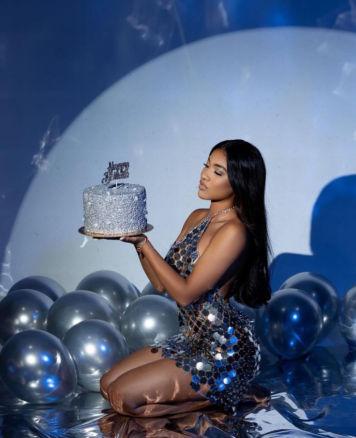 a woman sitting on the floor with a cake in front of her and balloons behind her