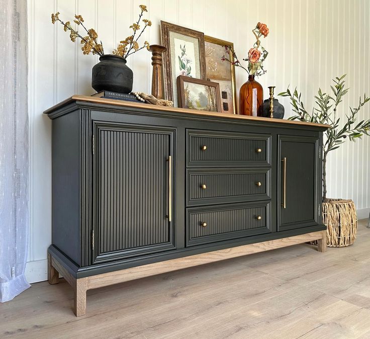 a black sideboard with drawers and vases on top in front of a white wall