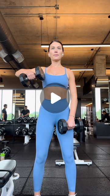 a woman holding two dumbs while standing in front of a gym equipment area with other people