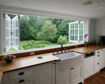 a kitchen with white cabinets and wooden counter tops next to a large window that looks out onto the yard