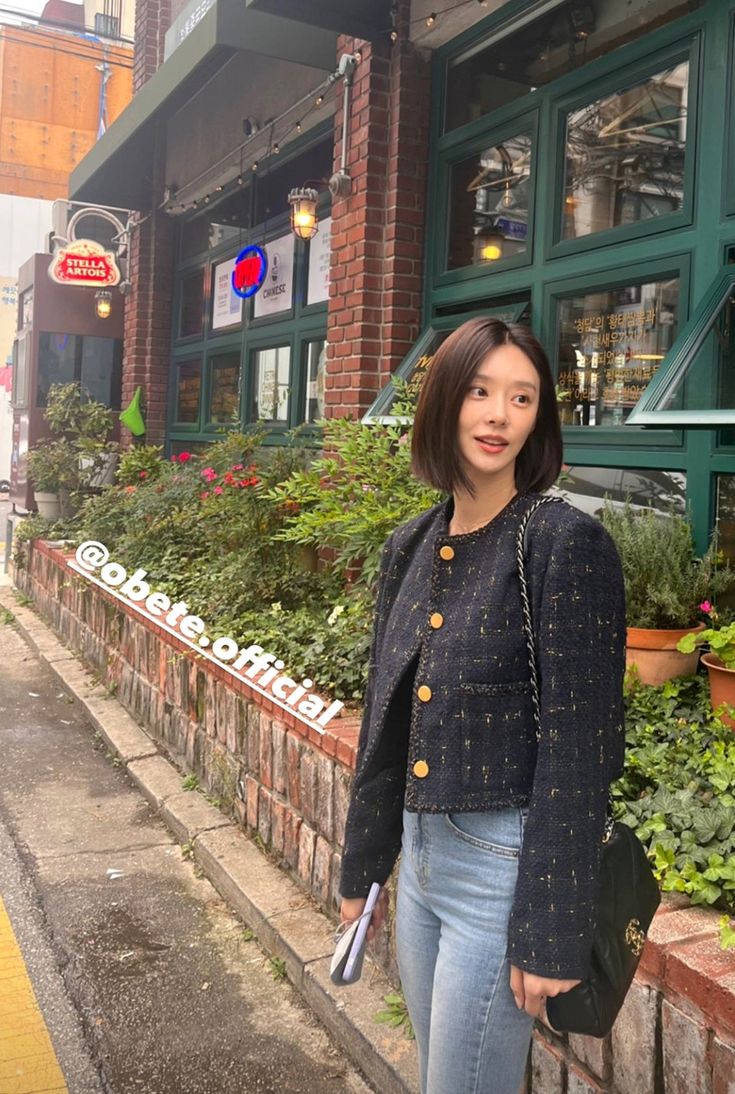 a woman standing on the sidewalk in front of a building with plants growing out of it