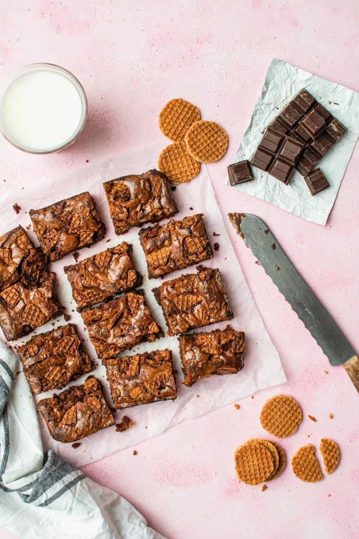 chocolate waffles and cookies on a pink surface next to a glass of milk