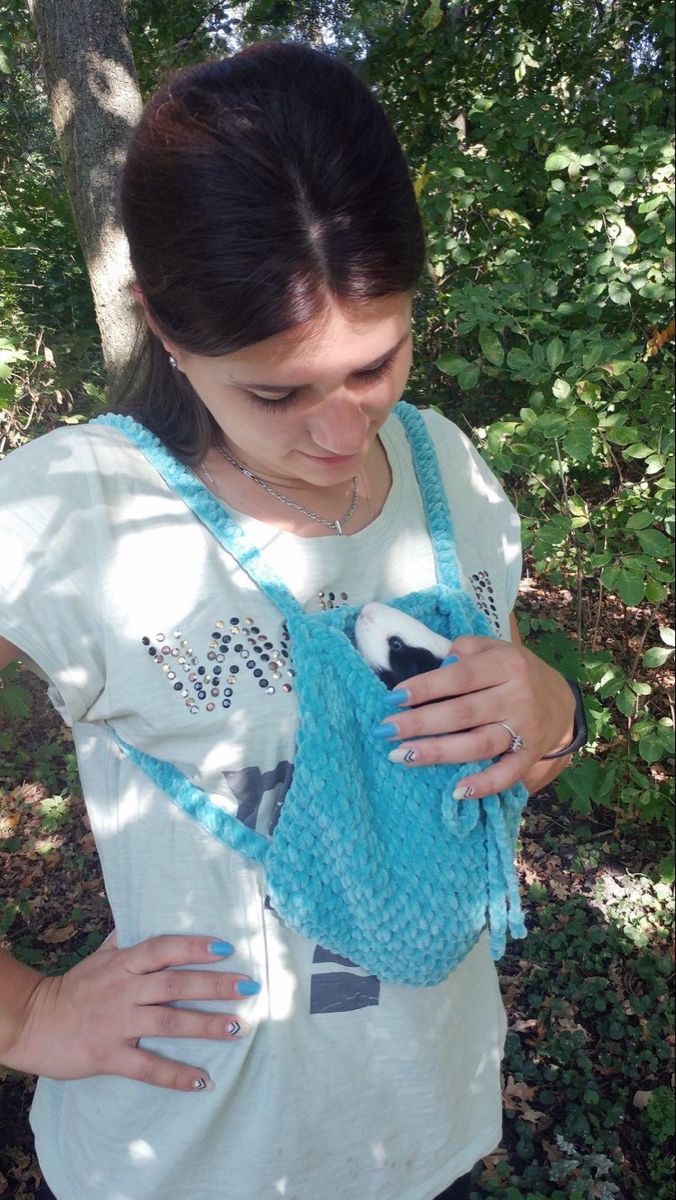 a woman is holding a blue knitted bag in front of some trees and bushes