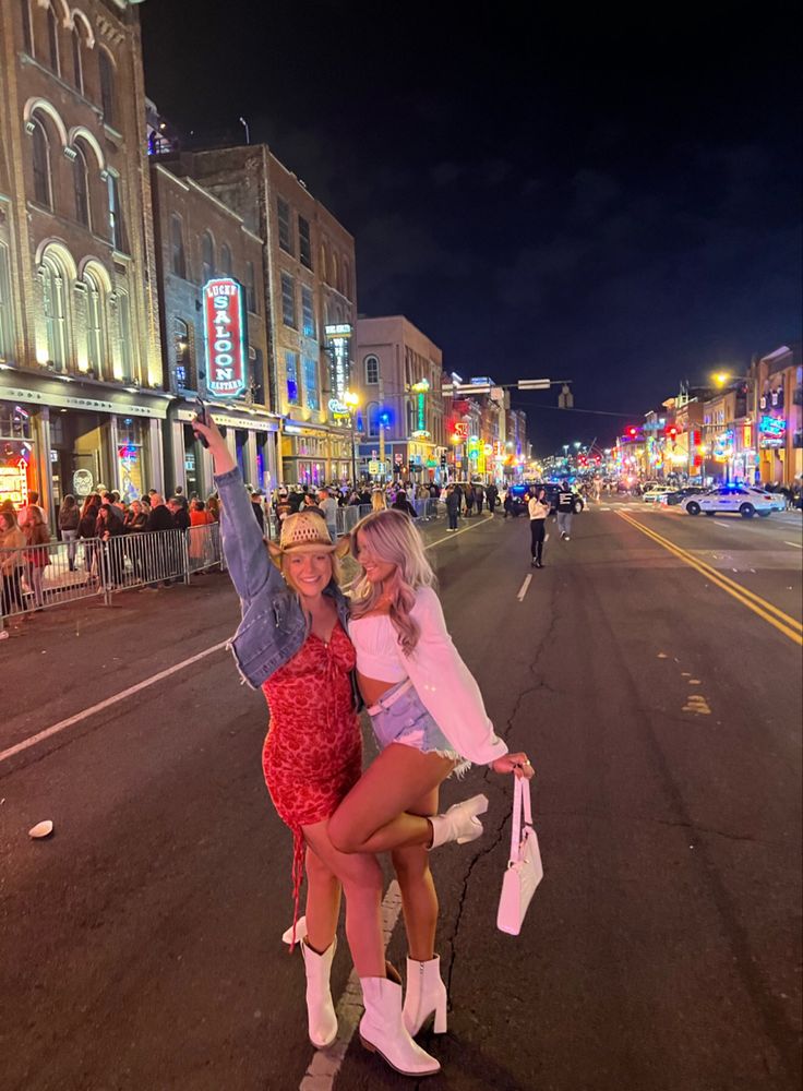 two women standing on the side of a road in front of tall buildings at night