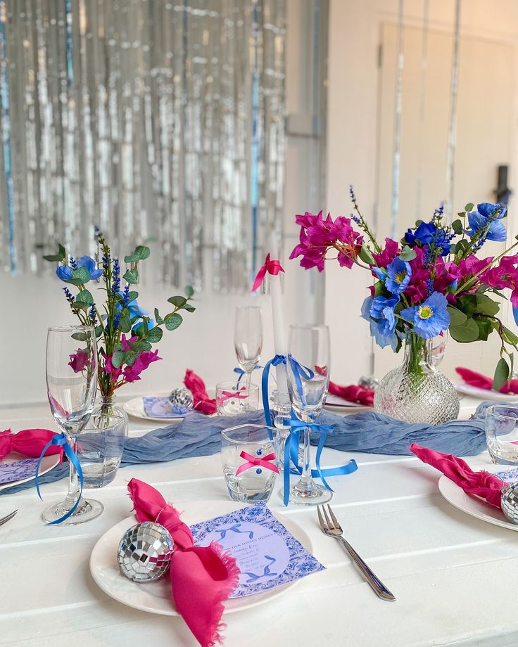 the table is set with pink, blue and white flowers