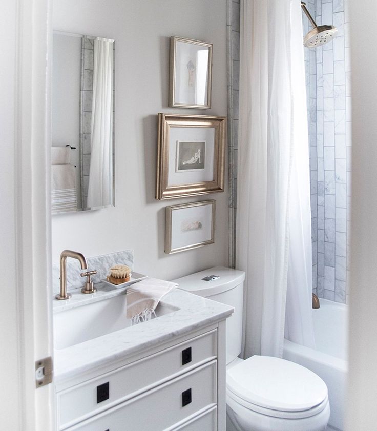 a white bathroom with gold framed pictures on the wall and a toilet next to it