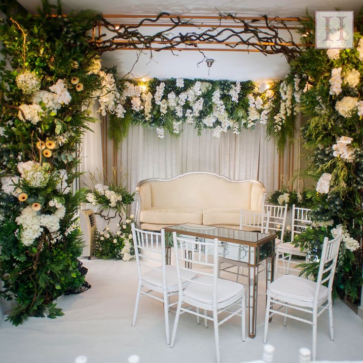 a table and chairs are set up for a wedding ceremony with flowers on the wall