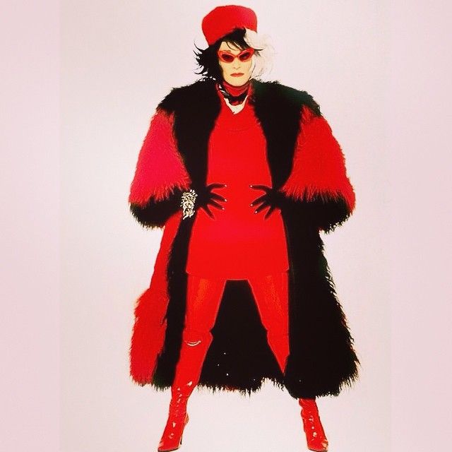 a woman dressed in red and black is standing with her hands on her hips while wearing a fur coat