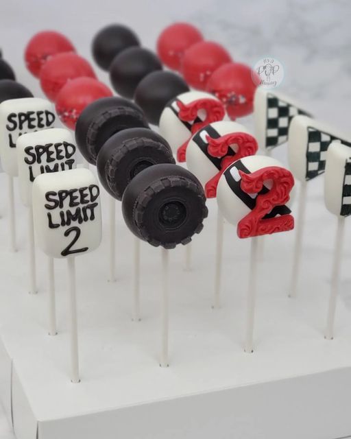 cake pops decorated with black and red racing cars are on top of a white stand