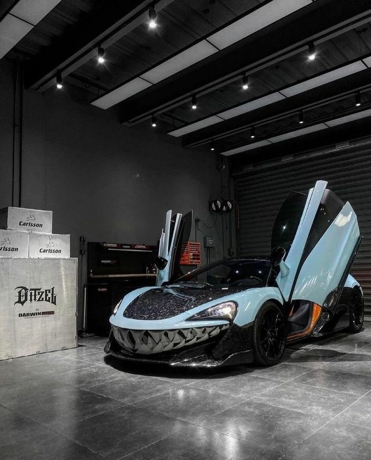 a blue and black sports car parked in a garage with its doors open to reveal the hood