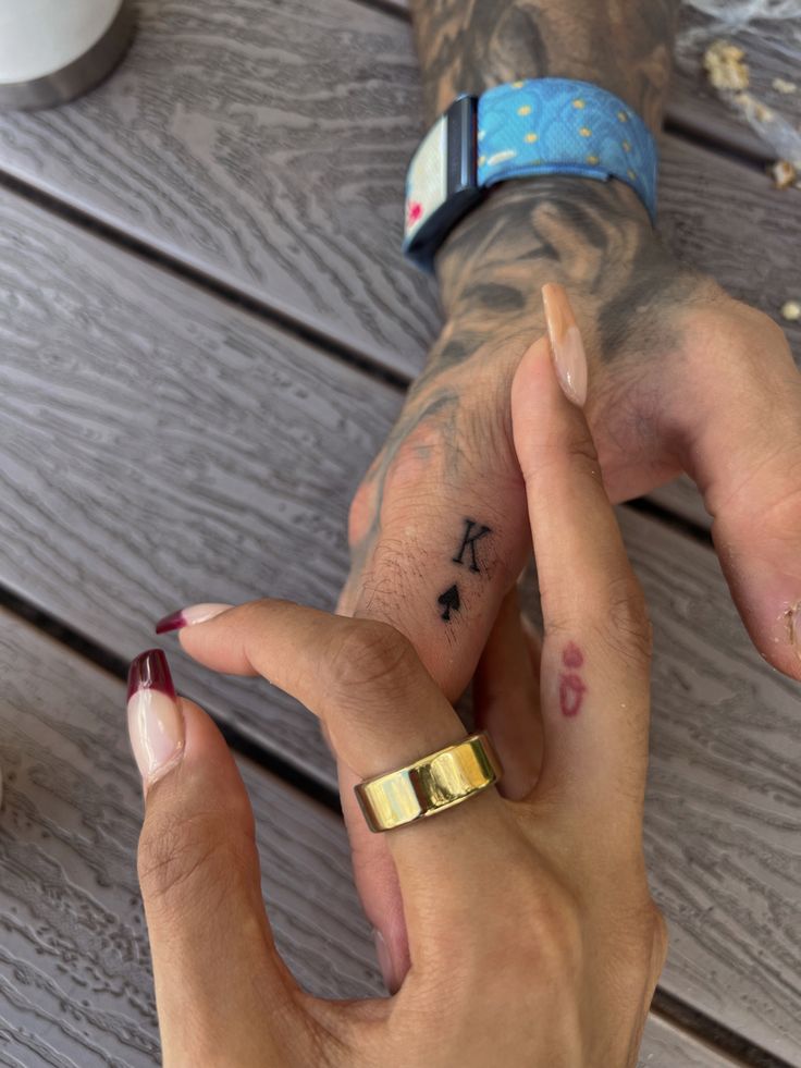 two people holding hands with tattoos on their fingers and one has a gold band around the other's wrist