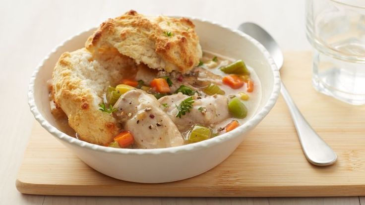 a bowl of chicken pot pie soup on a cutting board next to a glass of water