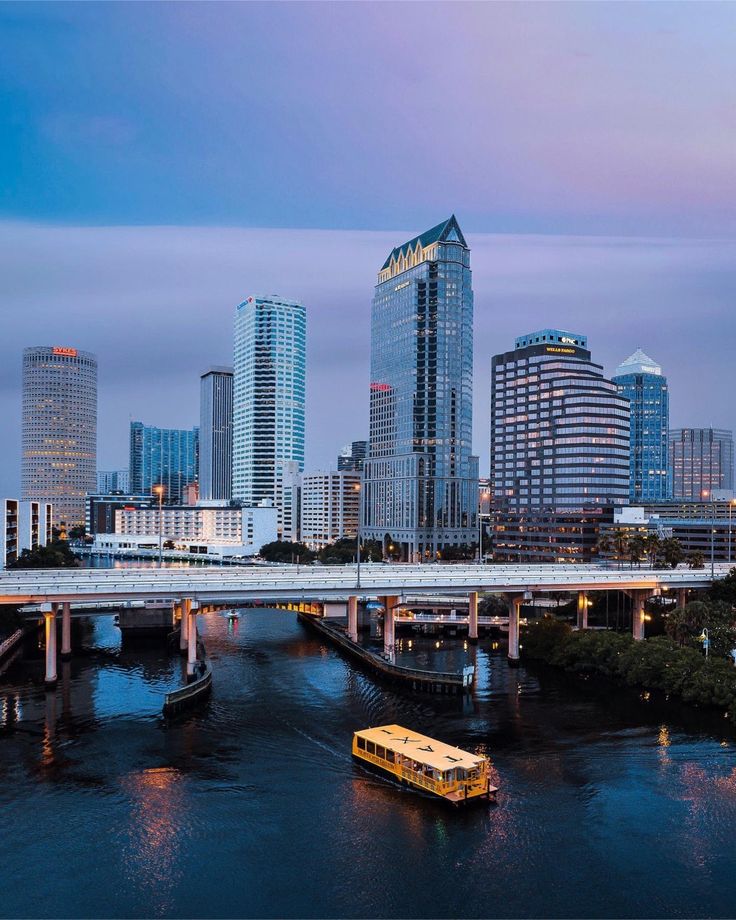 a bus is driving across a bridge over the water in front of some tall buildings